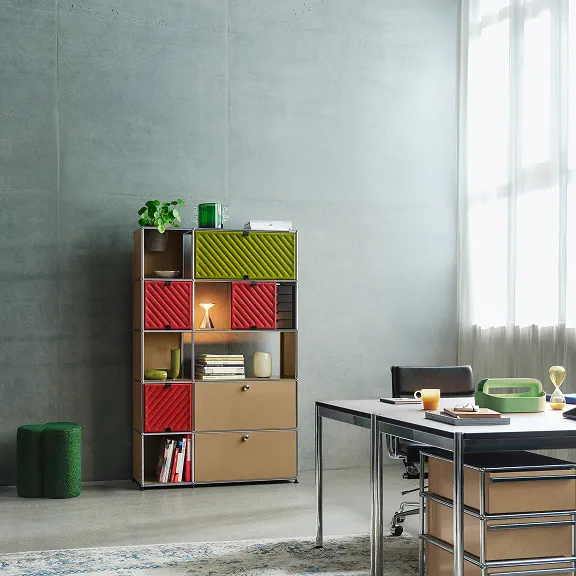 Im Hintergrund steht ein USM Haller Regal in USM Beige, es enthält USM Haller Soft Panels. Im Vordergrund sieht man einen Schreibtisch im Anschnitt.